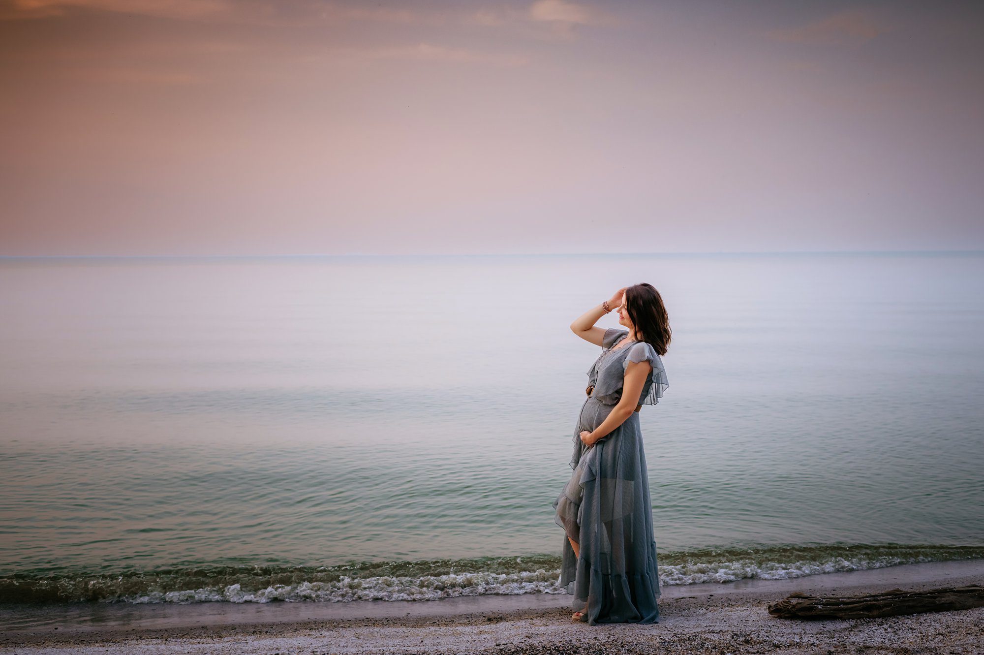 pregnant woman standing in front of lake at sunset