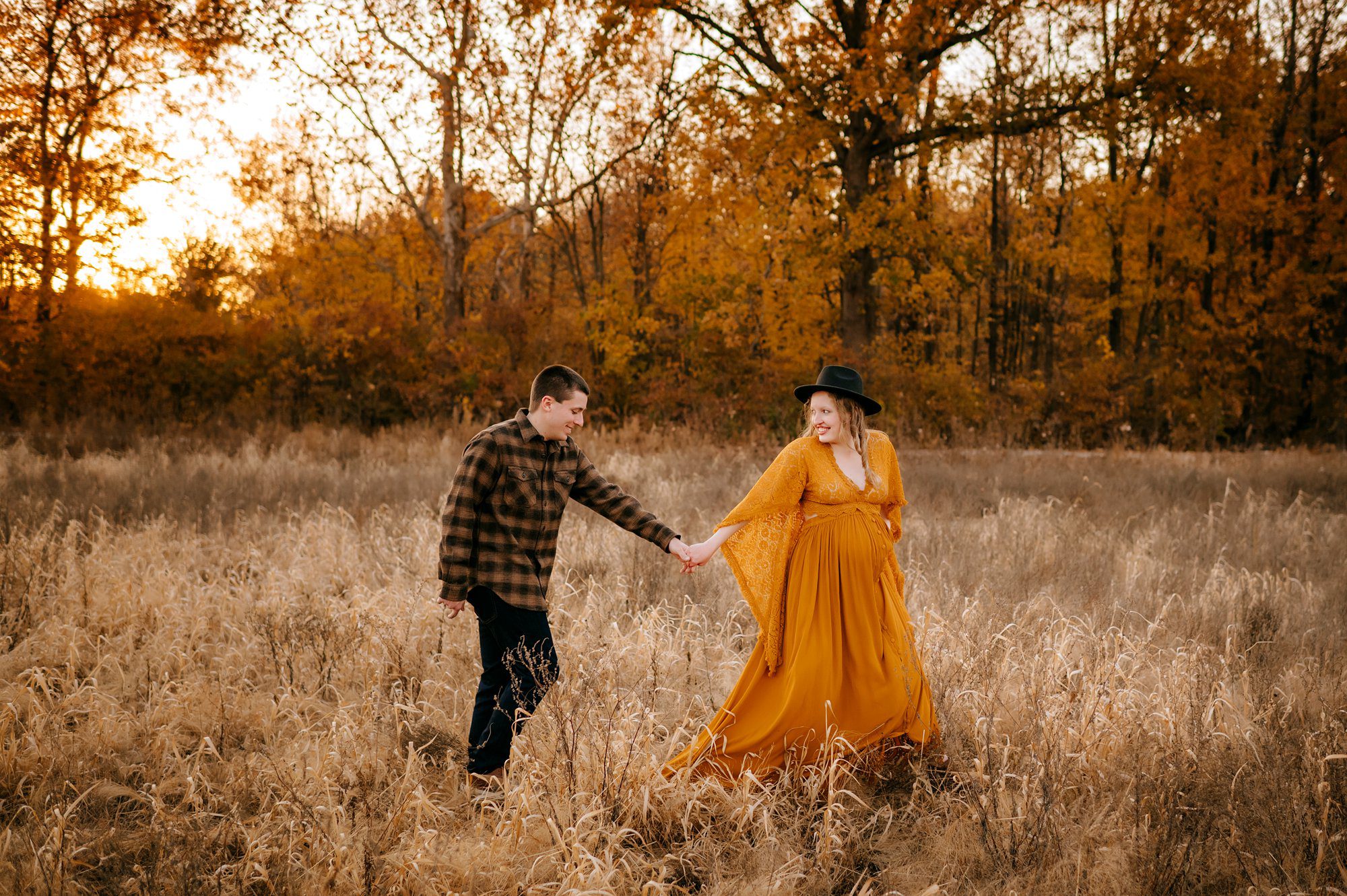 couple walking through fall field in mustard yellow dress with baby bump